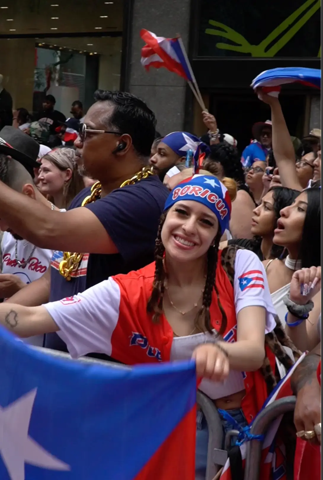 Fan in a Boricua bandana cheering at the parade barricade